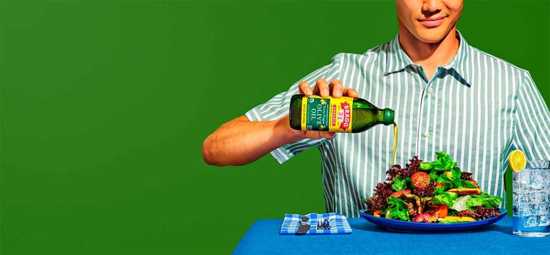 Person pouring Bragg olive oil on a salad